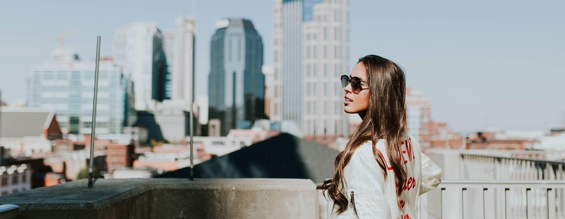 woman with sunglasses stands on a rooftop overlooking the city